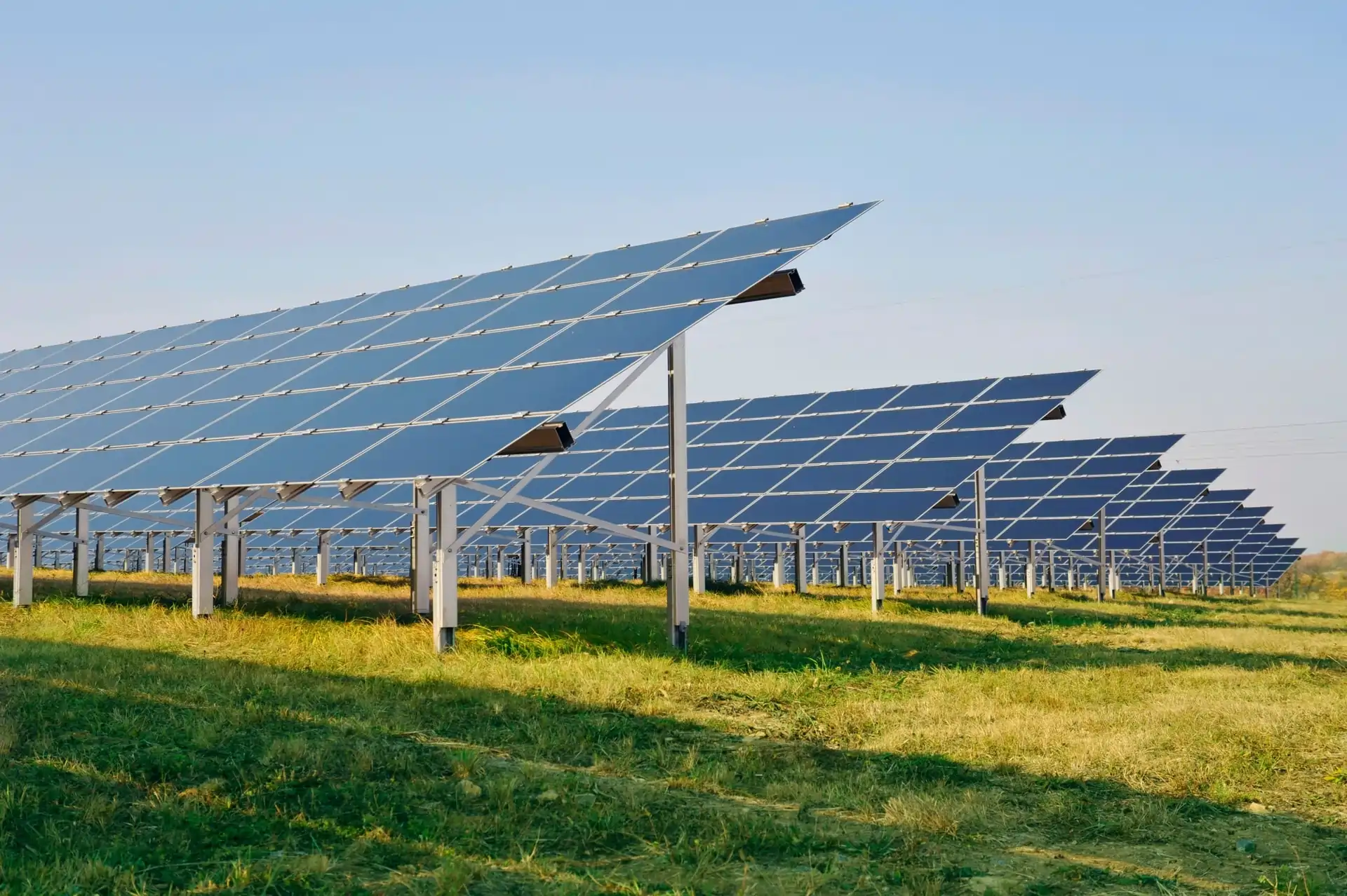 Solárne panely na kovových podperách umiestnené na zelenej lúke pod modrým nebom, znázorňujúce medzinárodné projekty v oblasti obnoviteľnej energie