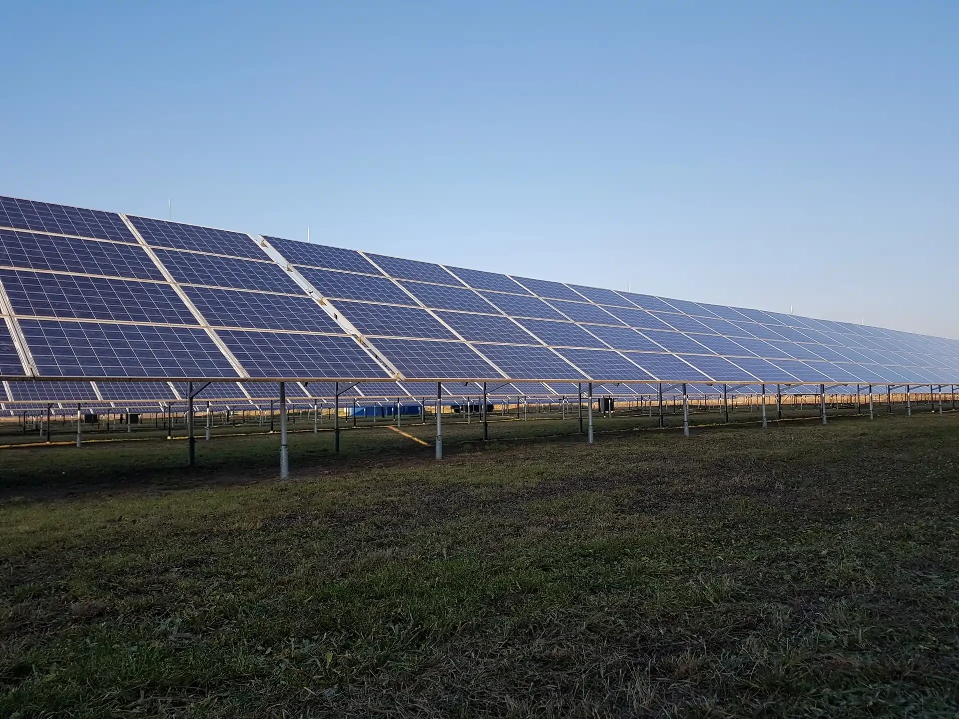 Rozsiahly solárny park s radmi solárnych panelov na kovových konštrukciách pod šedým nebom, používaný ako hlavné pozadie pre sekciu solárnych parkov