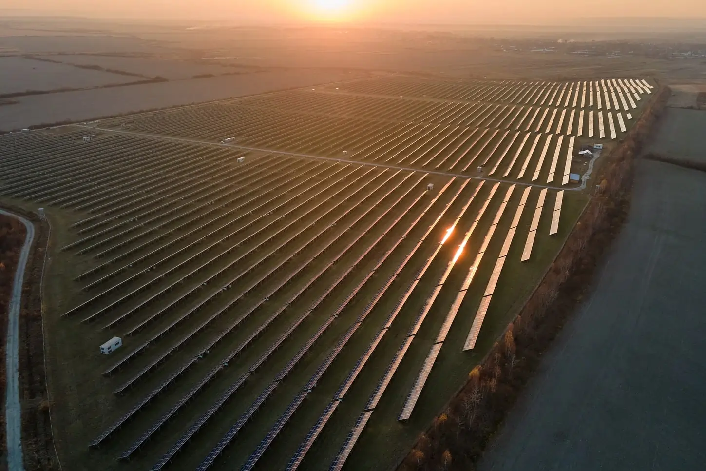 Letecký pohľad na rozsiahly solárny park s radmi solárnych panelov počas západu slnka, zobrazujúci veľkoplošnú solárnu elektráreň