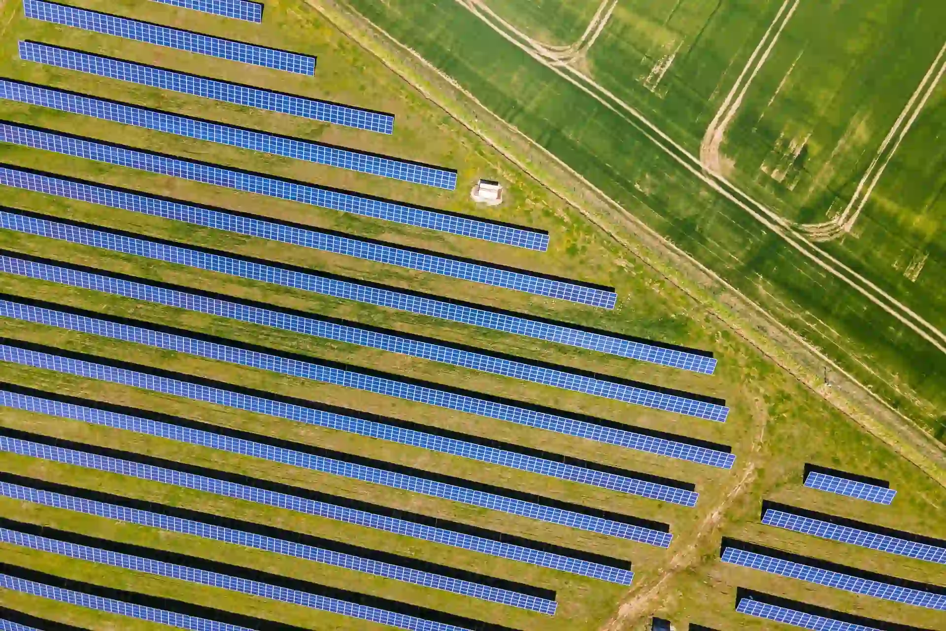 Letecký pohľad na solárny park Tekovské Nemce s modrými solárnymi panelmi usporiadanými v pravidelných radoch na zelenej krajine s cestami okolo, Správa energetických zariadení od green energy